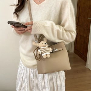Detail of khaki leather bucket bag with metal lock and cute plush dog charm