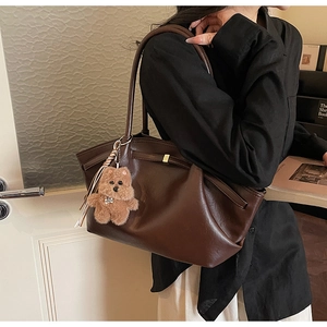 Model wearing dark brown faux leather tote bag with gold buckle and plush bear charm