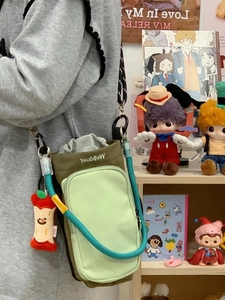 Two-tone green crossbody bag with adjustable braided strap and apple charm on a model