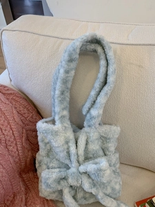 Blue and white plush tote bag with a large bow on a soft fabric sofa background