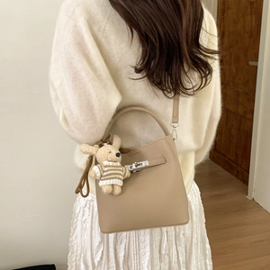 Detail of khaki bucket bag with metal twist lock and cute teddy bear charm