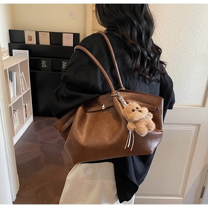 Detail of a brown leather tote bag with a gold metal buckle and a cute bear charm