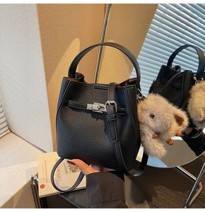 Close-up of black litchi grain leather bucket bag with metal buckle and plush charm detail