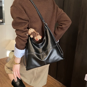 Detail of black hobo bag featuring white contrast stitching and a cute bear charm accessory