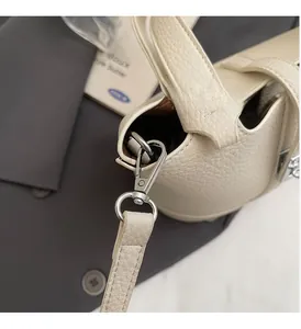 Close-up of silver metal hook and lychee texture leather strap on beige bucket bag