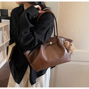 Macro shot of dark brown matte leather tote bag featuring gold buckle and plush bear charm