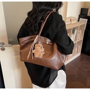 Brown leather tote bag featuring a decorative fringe strap and plush bear charm