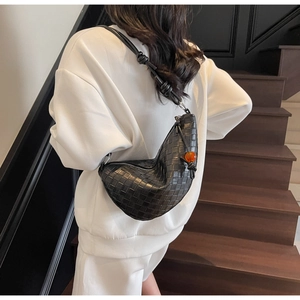 Détail du sac hobo en cuir tressé noir avec nœud et perle orange sur un sweat-shirt blanc
