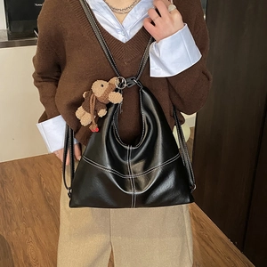 Detail of black tote bag featuring white contrast stitching and a plush bear pendant