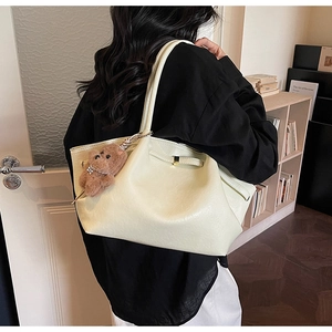 Detail of soft cream tote bag with metal closure and a cute brown plush bear charm