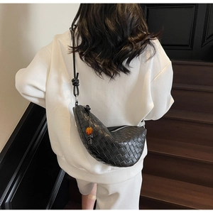 Détail d'un sac demi-lune en cuir tressé noir avec une perle orange sur la bandoulière fixe