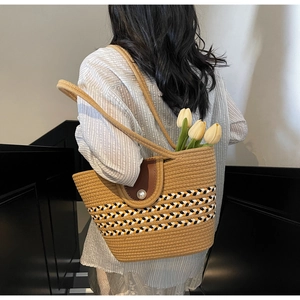 Detail of woven tote bag featuring a leather flap with a pearl closure and striped trim
