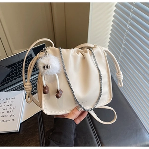 Close-up of beige ruched leather bag featuring a gold chain and plush monster charm