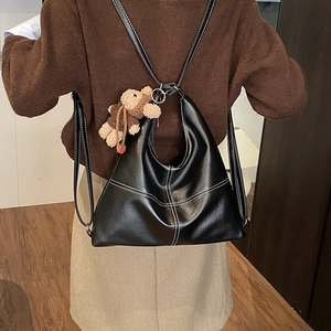 Detail of black PU leather tote with white stitching and bear charm worn as a backpack
