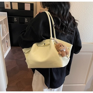 Detail of cream tote bag with metal buckle and brown plush bear charm on strap