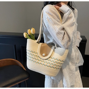 Detail of straw tote bag featuring colorful woven strap and faux pearl button closure