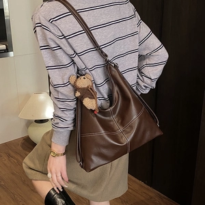 Detailed close-up of brown tote bag showing contrast white stitching and plush bear charm
