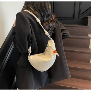 Detail of white woven crescent shoulder bag with orange bead and knotted strap design