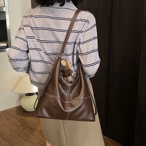 Detail of dark brown leather tote with contrast stitching and a cute bear plush charm