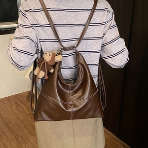 Detail view of large brown tote bag with contrast stitching and bear charm on model back