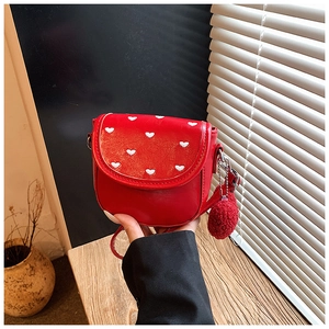 Dettaglio della borsa a sella rossa con cuori ricamati e un ciondolo pompon di peluche