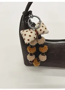 Close-up of plush ball bag charm with polka dot bow on dark brown leather handbag