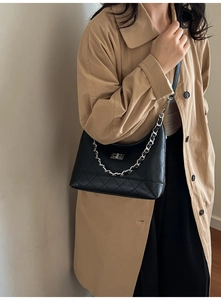 Détail d'un sac bandoulière noir matelassé avec chaîne argentée porté sur un trench-coat