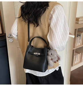 Detail of black lychee grain leather bucket bag with metal lock and plush bunny charm
