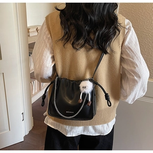 Detail of black pleated crossbody bag with plush monster charm and silver chain strap