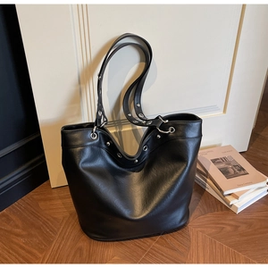 Close-up of black leather tote bag with silver eyelets on wooden parquet floor