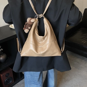 Detail of beige faux leather tote bag with teddy bear charm worn as a backpack