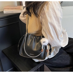 Close-up of black pleated crossbody bag with silver chain and white plush keychain