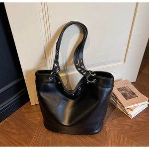 Detail of black faux leather tote bag showing silver metal eyelet studs and grainy texture