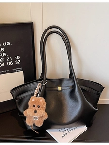 Minimalist black leather tote bag with long straps and cute dog charm in studio setting