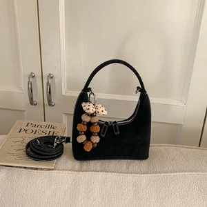 Close-up of black suede dumpling bag featuring white stitching and decorative bow charm