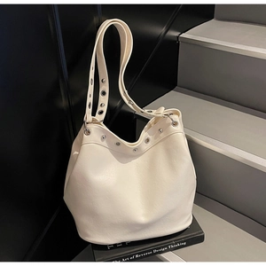 Close-up of cream textured leather tote bag with silver eyelet details on a black book