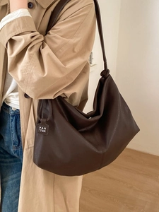 Large dark brown leather tote bag with PAN'TOR tag shown on shoulder with khaki trench coat