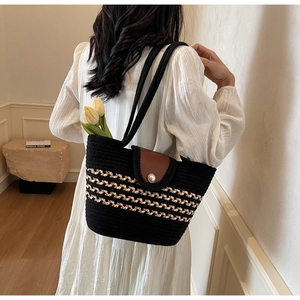 Detail of hand-woven black straw tote with pearl buckle and brown leather flap