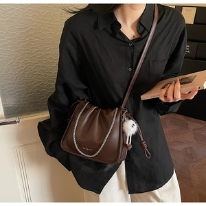 Detail of dark brown leather crossbody bag with pleated texture and gold chain link strap