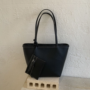 Detail of black pebbled leather tote with white contrast stitching and a small pouch