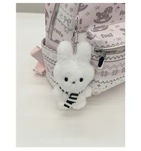 Detail of soft white plush rabbit charm with striped scarf on a stylish backpack