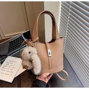 Detail of light brown lychee grain leather bucket bag with silver lock and plush bunny charm