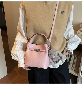 Detail of pink lychee leather bucket bag with top handle and plush bunny charm