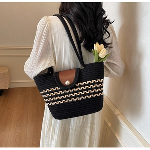 Detail of woven tote bag with brown leather flap and pearl clasp on a model shoulder
