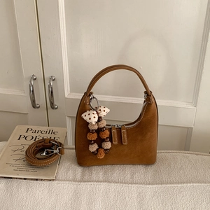 Detail of brown suede hobo bag featuring decorative zippers and fluffy pompom charm
