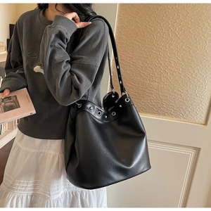 Detail of high-capacity black tote bag with glossy leather texture and silver eyelets