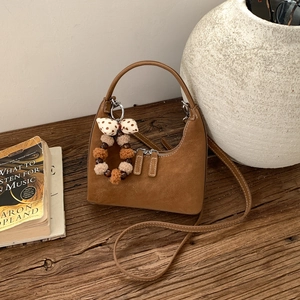 Detailed view of a brown suede half-moon bag with decorative pompom and bow charm