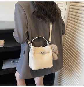 Close-up of beige lychee leather bucket bag with silver twist lock and bear charm