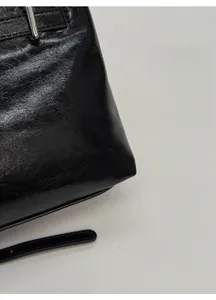 Gros plan détaillé du cuir noir plissé brillant et boucle argentée d'un sac à bandoulière