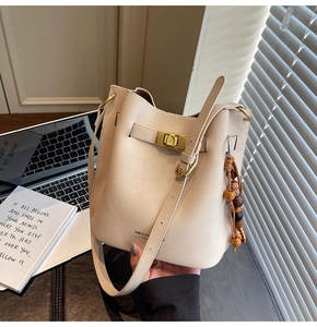 Détail d'un sac seau en cuir crème avec fermoir rotatif doré et charm en perles de bois